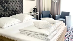 Ett hotellrum med en stor säng, ett nattduksbord med en lampa, en stol och en inramad tavla på väggen.