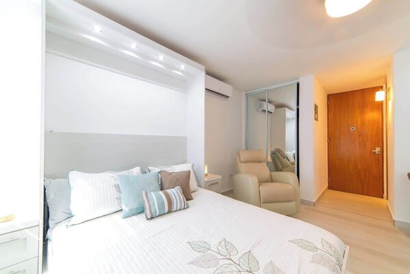 A bedroom with a bed, a chair, a wooden door, and a mirror.