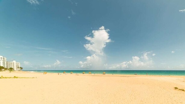Ein weiter Sandstrand mit blauem Himmel und vereinzelten Wolken.