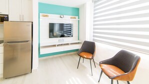 Eine moderne Küche mit einem Edelstahl-Kühlschrank, einem Flachbildfernseher an einer türkis farbenen Akzentwand und zwei Stühlen mit Ledersitzen.