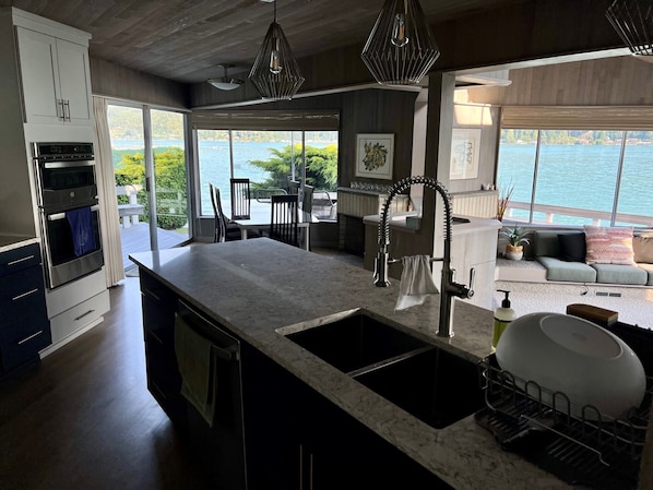 A modern kitchen with a large island, built-in oven, and a view of a lake.