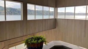 Ein Zimmer mit großen Fenstern und Blick auf See und Wald.