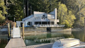 Ein modernes Haus mit einer Anlegestelle, die in einen stillen See führt, umgeben von Bäumen.