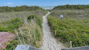Un sendero arenoso que conduce a una playa, con un cartel que advierte sobre el peligro de pisar las dunas.