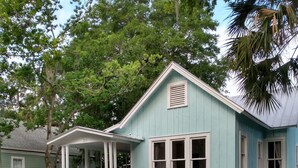 Uma casa azul clara com varanda, cerca branca de piquetes e o número '214' na varanda.