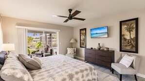Une chambre à coucher comprenant un lit, une commode, une chaise, un ventilateur de plafond et un téléviseur.