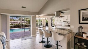 Une cuisine moderne dotée d’un grand îlot central, de tabourets de bar et offrant une vue sur l’espace piscine.