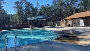 Una piscina con zona techada y sillas de descanso, rodeada de árboles.