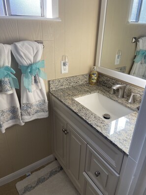 A bathroom with a granite countertop sink, a mirror, and two towels with blue bows. - Pier Serenity Waterfront! (Huntsville)