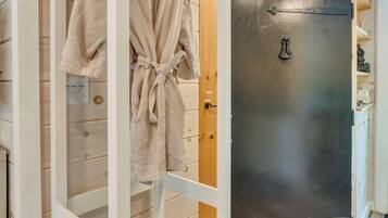 A white wardrobe with a hanging robe and slippers, a black door with a handle, and a wooden floor.