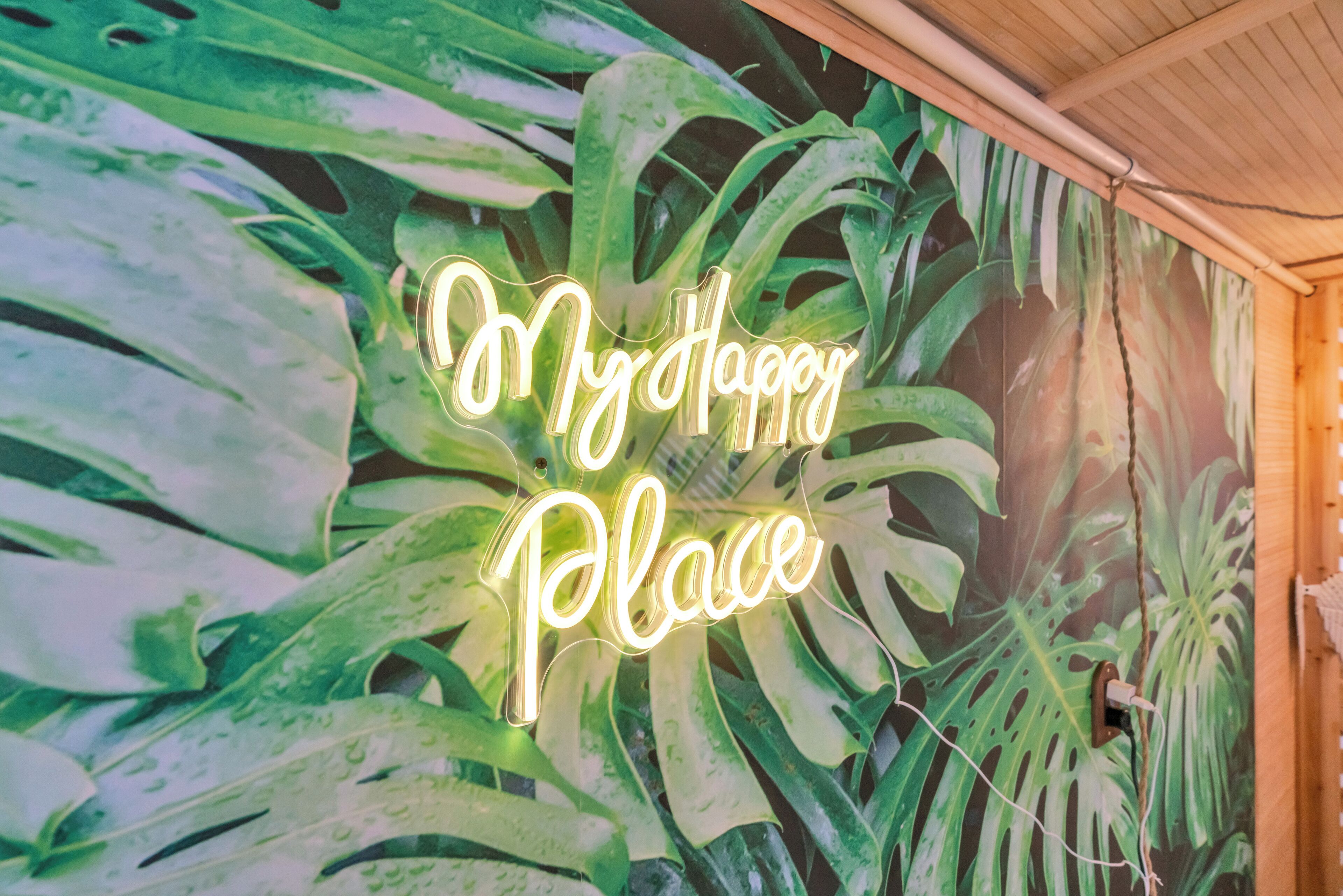 A neon sign that reads "My Happy Place" against a backdrop of green foliage.