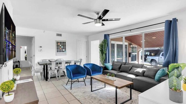 A modern living room with a sofa, two blue armchairs, a coffee table, a dining area with a table and chairs, and a ceiling fan. - Pool + Game Room 4BR · Cheerful Hollywood Getaway (Hollywood)