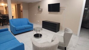 Ein modernes Wohnzimmer mit einem blauen Sofa, grauen Sessel, einer schwarzen Unterhaltungsanlage und einem Deckenventilator.