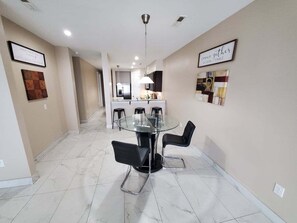 A modern dining area with a glass table and black chairs, a kitchen in the background, and a hallway leading to other rooms. - Gone Coastal 3 BR Direct Oceanfront  (Myrtle Beach)