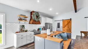 Une cuisine moderne avec des meubles blancs, un îlot central en bois et une porte de style champêtre.