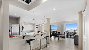 A modern kitchen with a central island, bar stools, and a dining area with a view. - Ocean Pearl: 7 BR Oceanfront Condo (Myrtle Beach)