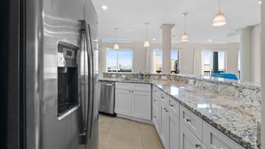 A modern kitchen with stainless steel appliances, white cabinetry, granite countertops, and pendant lighting. - Ocean Pearl: 7 BR Oceanfront Condo (Myrtle Beach)