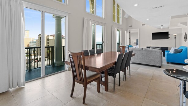 A spacious living area with a dining table, sofas, and a balcony with a view of the city. - Ocean Pearl: 7 BR Oceanfront Condo (Myrtle Beach)