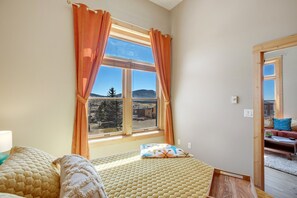 A bedroom with a large window, a bed with a quilted cover, and a view of a landscape. - Page 1-Mid-Century Modern With Mountain View (Victor)
