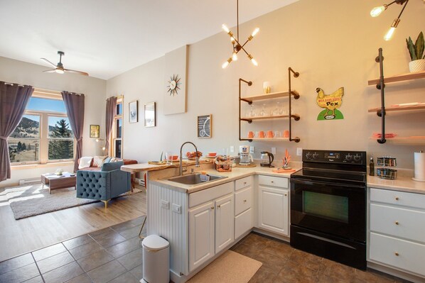 A modern kitchen with white cabinets, a black stove, and a dining area with a blue sofa and a wooden table. - Page 1-Mid-Century Modern With Mountain View (Victor)