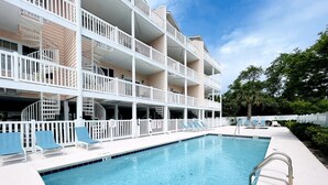 A swimming pool with a white deck, lounge chairs, and a multi-story building with balconies. - Great 7 BD walk to the beach + pool (North Myrtle Beach)
