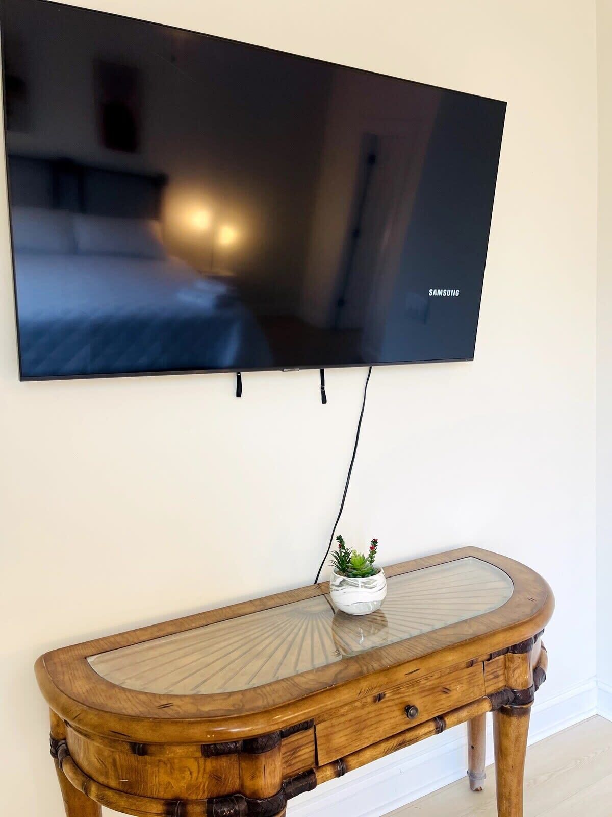 Un televisor de pantalla plana montado en la pared sobre un mueble bajo de madera con tapa de cristal y una pequeña planta en maceta.