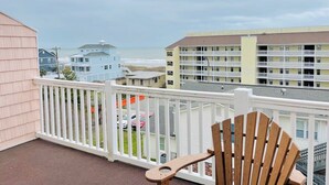 A balcony with a wooden chair, overlooking a beach and buildings. - Great 7 BD walk to the beach + pool (North Myrtle Beach)