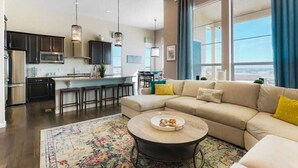 Ein modernes Wohnzimmer mit einer großen Couch, einem Couchtisch und einer Küche im Hintergrund.