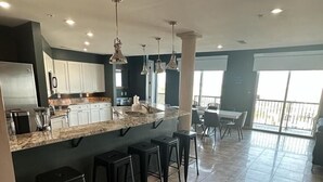 Una cocina moderna con encimera de mármol, taburetes de bar negros e iluminación colgante.