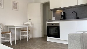 Een kleine keuken met witte keukenkastjes, een inbouwoven en een koffiezetapparaat.
