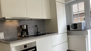 Een moderne keuken met witte kasten, een inbouwoven, een koffiezetapparaat en een magnetron op het aanrecht.
