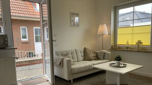 Een moderne woonkamer met een beige bank, een witte salontafel en een raam met gele jaloezieën.
