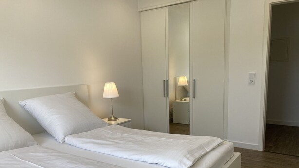 Een hotelkamer met een bed, nachtkastje, lamp, kast en een spiegel.
