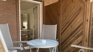 Een buitenpatio met een ronde glazen tafel en vier metalen stoelen.
