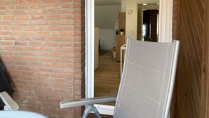 Een kamer met een bakstenen muur, een schuifdeur naar een andere kamer en een stoel met metalen frame.