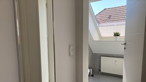 Een smalle gang met dakraam, leidend naar een balkon met betegeld dak en een bloempot.