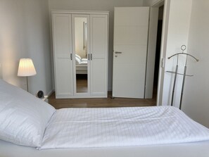 Et soveværelse med seng, natbord, lampe, garderobeskab og en dør til et andet rum.
