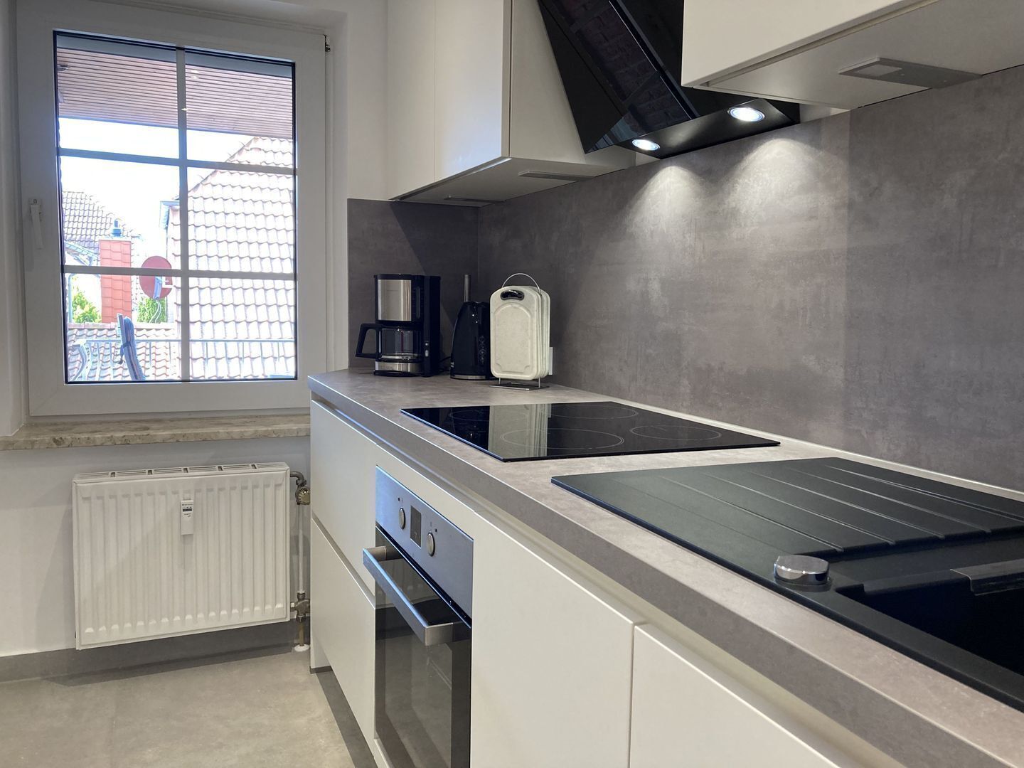 A modern kitchen with a built-in stove, a coffee maker, and a kettle on the countertop.