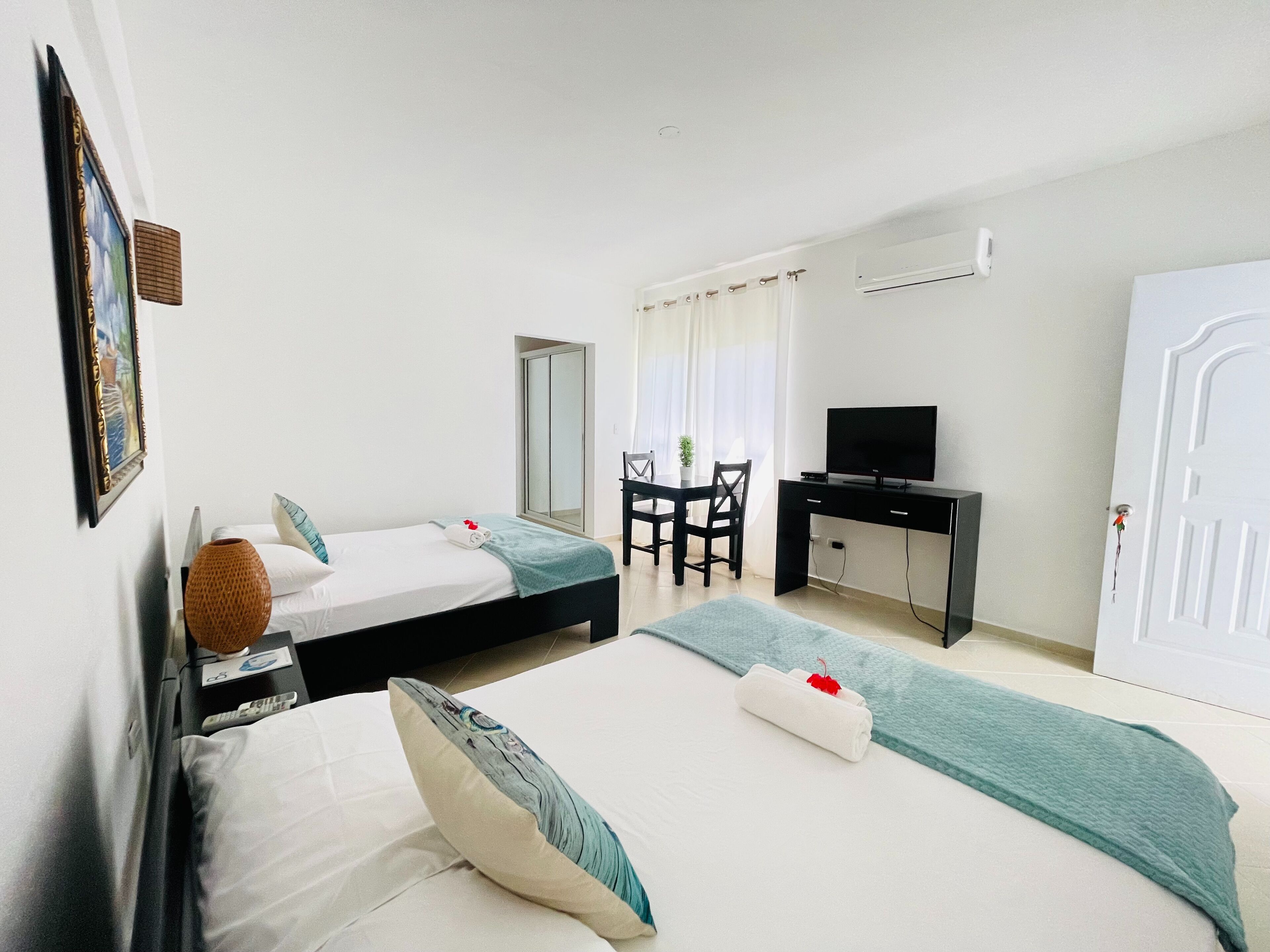 Habitación de hotel con dos camas, un escritorio con televisor, un armario y una ventana con cortinas.
