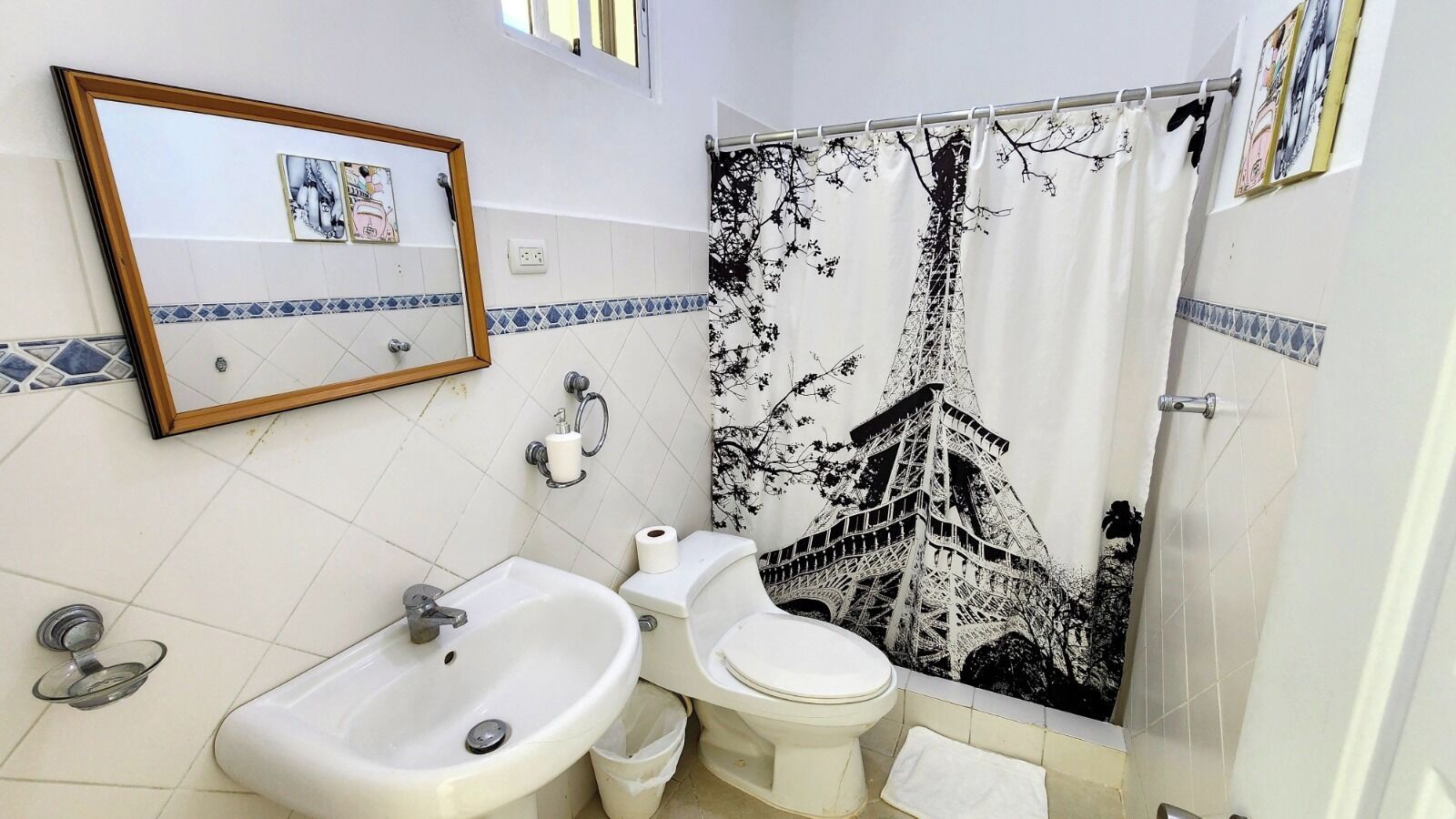 Une salle de bain équipée d’un lavabo, de toilettes et d’un rideau de douche orné d’un motif représentant la Tour Eiffel.