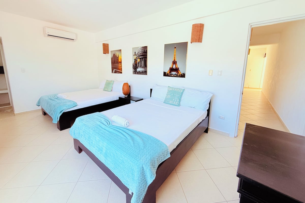A hotel room with two beds, a small table, and artwork on the walls.
