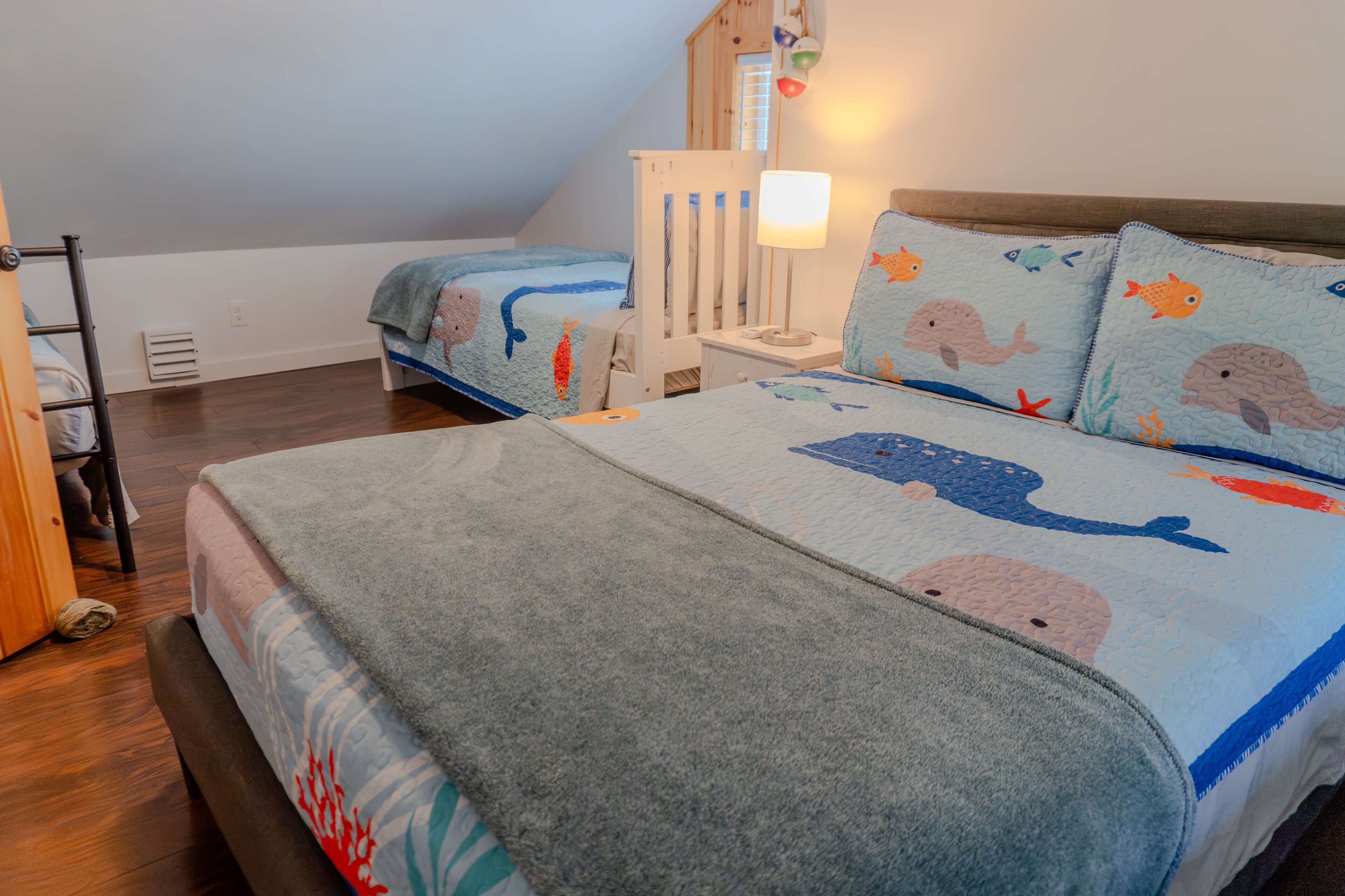 Ein Schlafzimmer mit zwei Betten, beide mit einer blauen und weißen Bettdecke im Meeresstil. Dazwischen steht ein weißer Nachttisch mit einer Lampe.