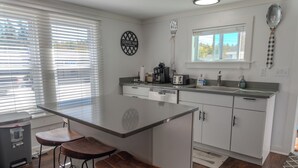 Cozinha moderna com ilha central, banquetas, cafeteira e torradeira.