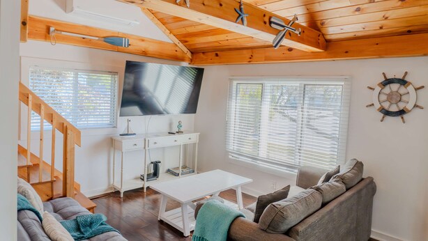 Sala de estar com teto de madeira, TV, sofá, mesa de centro e decoração com roda de barco.