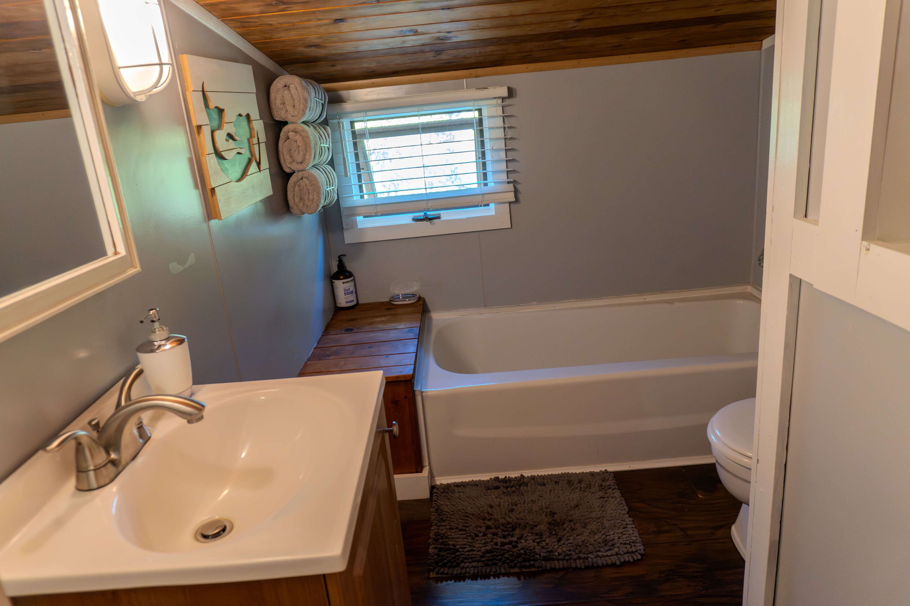 Un baño con tocador de madera, lavamanos, bañera y ventana con persianas.