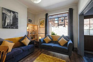 Un salon avec deux canapés, une petite table, une bibliothèque et une grande fenêtre donnant sur un immeuble en briques.