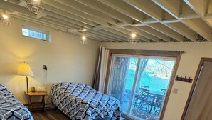 Un dormitorio con una cama grande, una cama más pequeña, un sofá, una lámpara y una ventana con vistas al exterior.