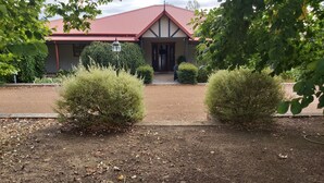 A building with a red roof, a front door, and a pathway leading to it. There are two bushes in the foreground. - Beautiful room, a comfy king bed, includes a delicious continental breakfast. (Balingup)