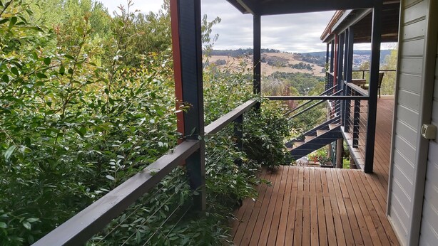 A wooden deck with a metal railing leading to a covered area with a view of a hilly landscape. - Beautiful room, a comfy king bed, includes a delicious continental breakfast. (Balingup)