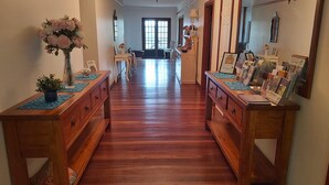 A hallway with wooden floors, flanked by two wooden desks with decorative items and framed pictures. - Beautiful room, a comfy king bed, includes a delicious continental breakfast. (Balingup)